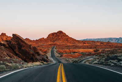 Country road leading towards mountains against clear sky during sunset