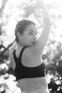 Portrait of teenage girl with arms raised standing against trees in park