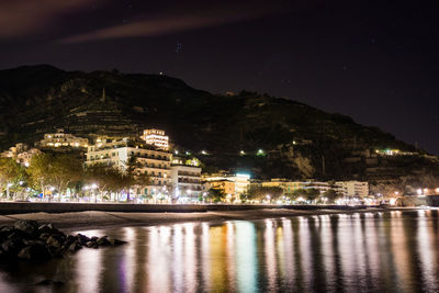 Illuminated city by river against sky at night