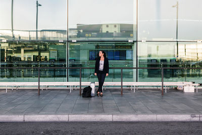 Female tourist with suitcase and backpack standing in airport and looking away while enjoying summer weekend