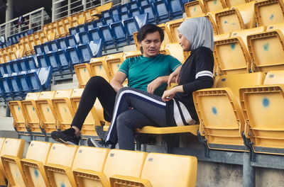 Athletes talking while sitting on chairs at stadium