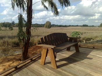 Empty wooden bench on field against sky