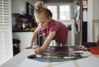 Girl painting on paper while standing by table at home