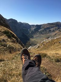 Low section of man on grass against mountains and sky