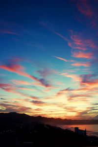 Silhouette of city against cloudy sky during sunset