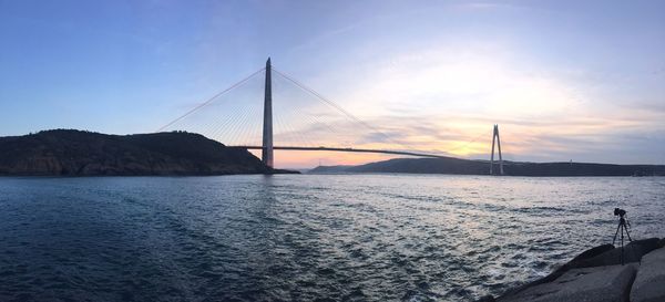 Suspension bridge over sea against sky during sunset