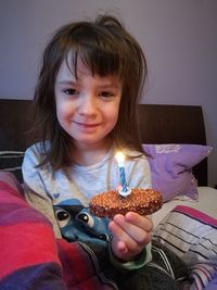 Portrait of smiling girl holding birthday cake while sitting on bed