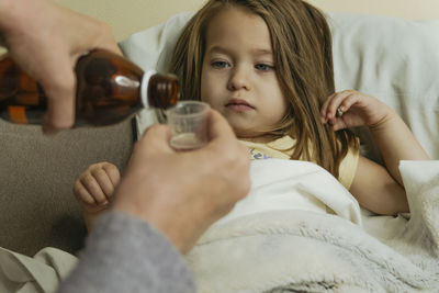 Female hands pour medicine for sick little girl
