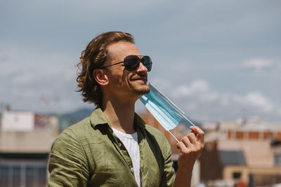 Portrait of young man drinking sunglasses against sky