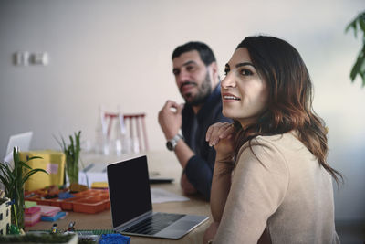 Female and male engineers looking away while sitting at table in office