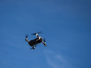 Low angle view of drone flying against blue sky