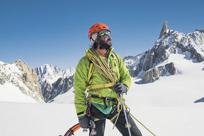 Hiker with climbing equipment standing on snow covered mountain against clear blue sky