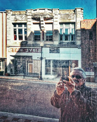 Reflection of man photographing building in city