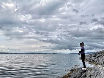 Woman fishing in sea against sky