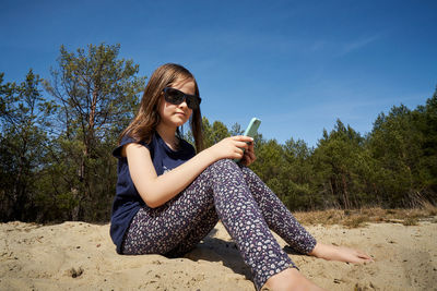 Cute little girl holds phone in hand and sits in summer forest