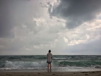 Rear view of man standing on beach against sky