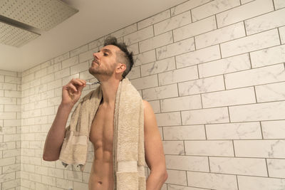 Shirtless man shaving in bathroom