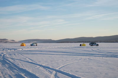 Winter lake with tents and cars of fishermens against the background of mountains.