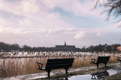 Deck chairs by lake against sky