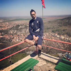 Full length of man sitting on railing against sky