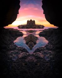 Scenic view of rock formations at beach against dramatic sky during sunset