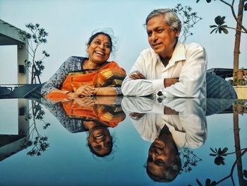 Smiling senior couple sitting by table with reflection