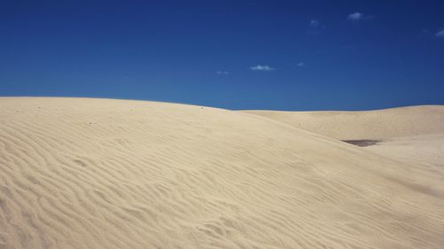Sand dunes in desert against blue sky