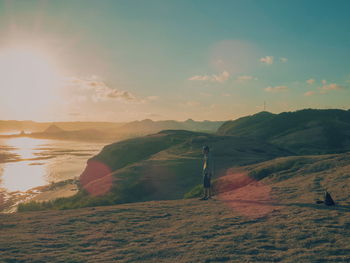 Man standing on hill by sea against sky during sunset
