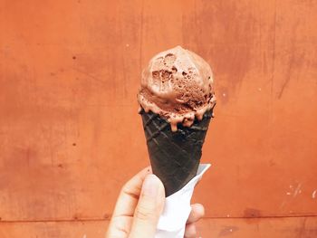 Hand holding ice cream cone against wall