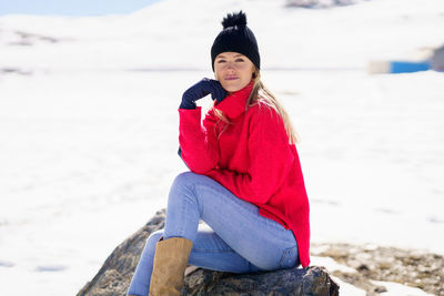 Young woman sitting on rock at beach during winter