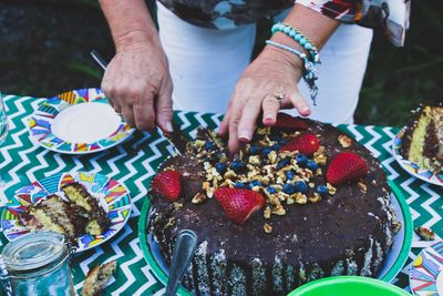 Midsection of woman cutting birthday cake on table