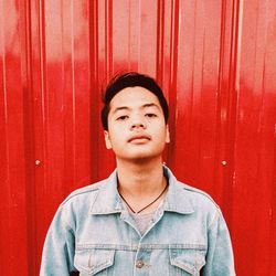 Portrait of young man standing against red wall