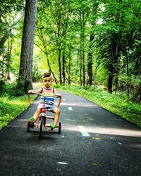 Portrait of boy riding tricycle on road in forest