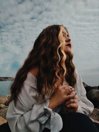 Young woman looking away while sitting against sky