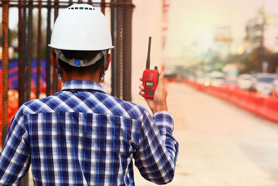 Rear view of man holding hat standing outdoors