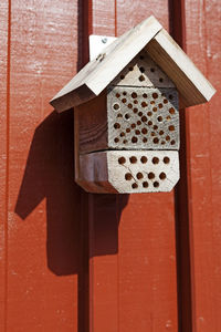 An insect hotel hanging on a red wooden wall