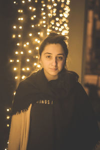 Portrait of young woman standing against illuminated wall