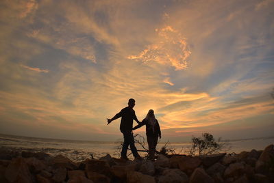 Men standing on rocks by sea against sky during sunset