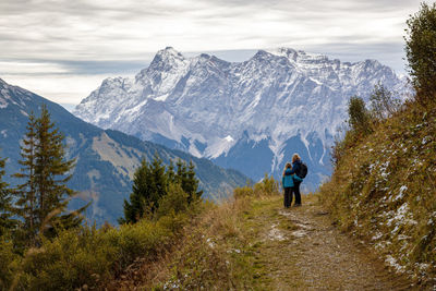 Rear view of man walking on snowcapped mountains against sky