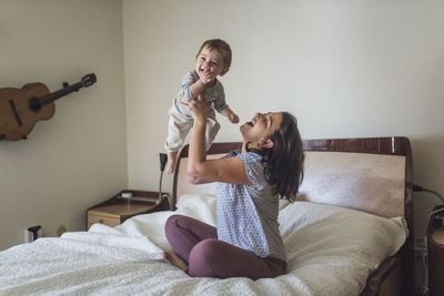 Mom holding laughing baby in the air in bedroom with guitar on wall