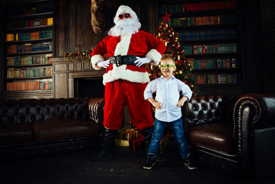 Full length of boy with santa clause standing at home