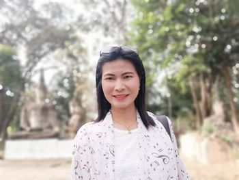 Portrait of smiling woman standing against trees