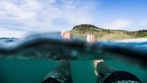 Low section of person swimming in sea against sky