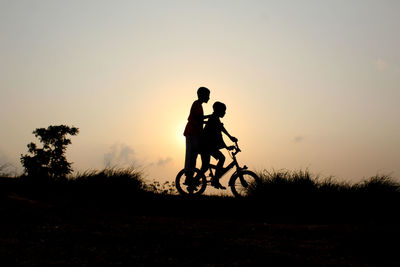 Silhouette of boys on bicycle against sky during sunset