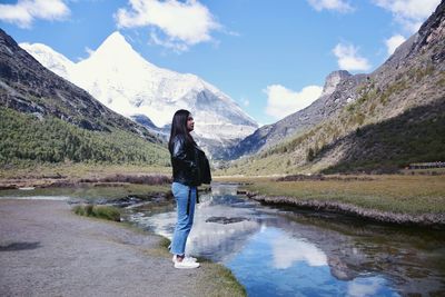 Full length of woman standing on land by river and mountain against sky