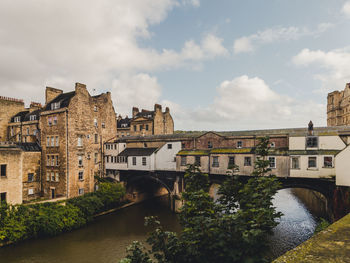 Arch bridge over river amidst buildings in city against sky