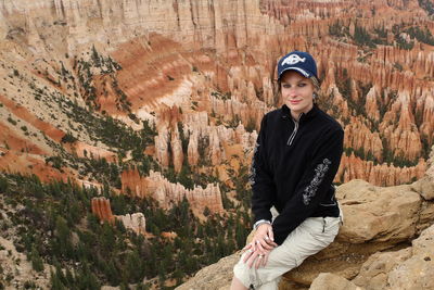 Portrait of woman sitting on cliff against dramatic landscape