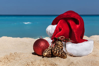 Bauble and santa hat on shore at beach during sunny day