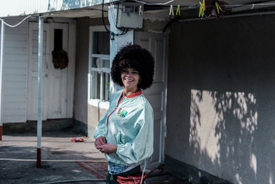 Portrait of smiling young woman with curly hair standing by building