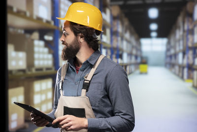 Portrait of young man using mobile phone while standing in factory